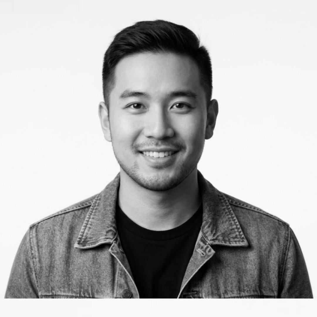 Professional black and white portrait of a smiling Jones Pham wearing a denim jacket and a black t-shirt against a clean white background.